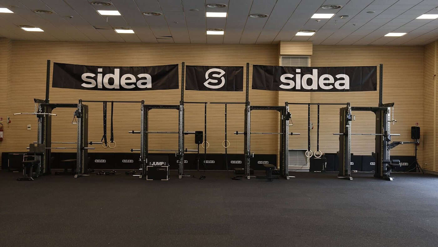 Piattaforma di presentazione con relatori e pubblico in una sala fitness professionale, attrezzature Sidea per eventi e conferenze di alta qualità.