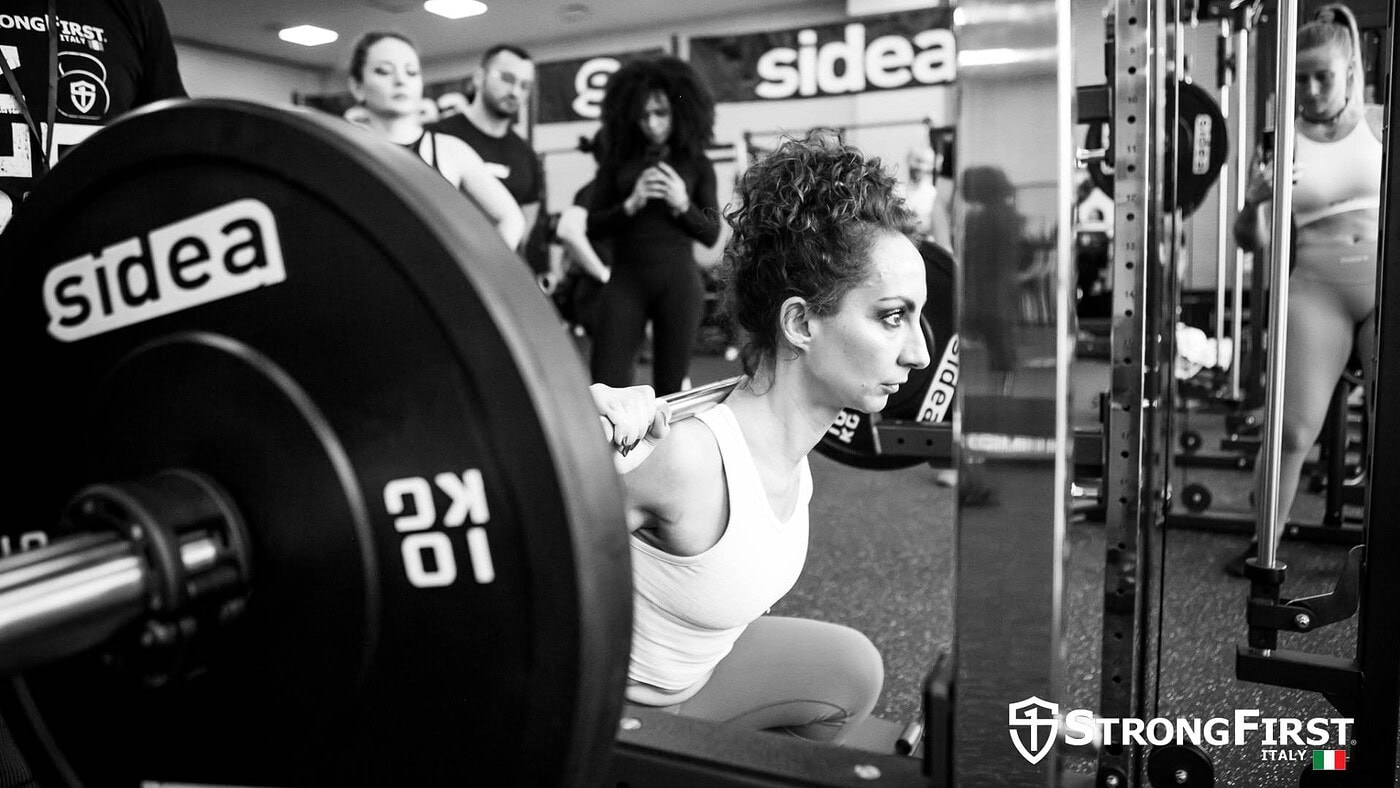 Pianista che esegue squat con bilanciere in palestra, evidenziando l'importanza di attrezzature fitness di alta qualità per allenamenti personalizzati e efficaci.