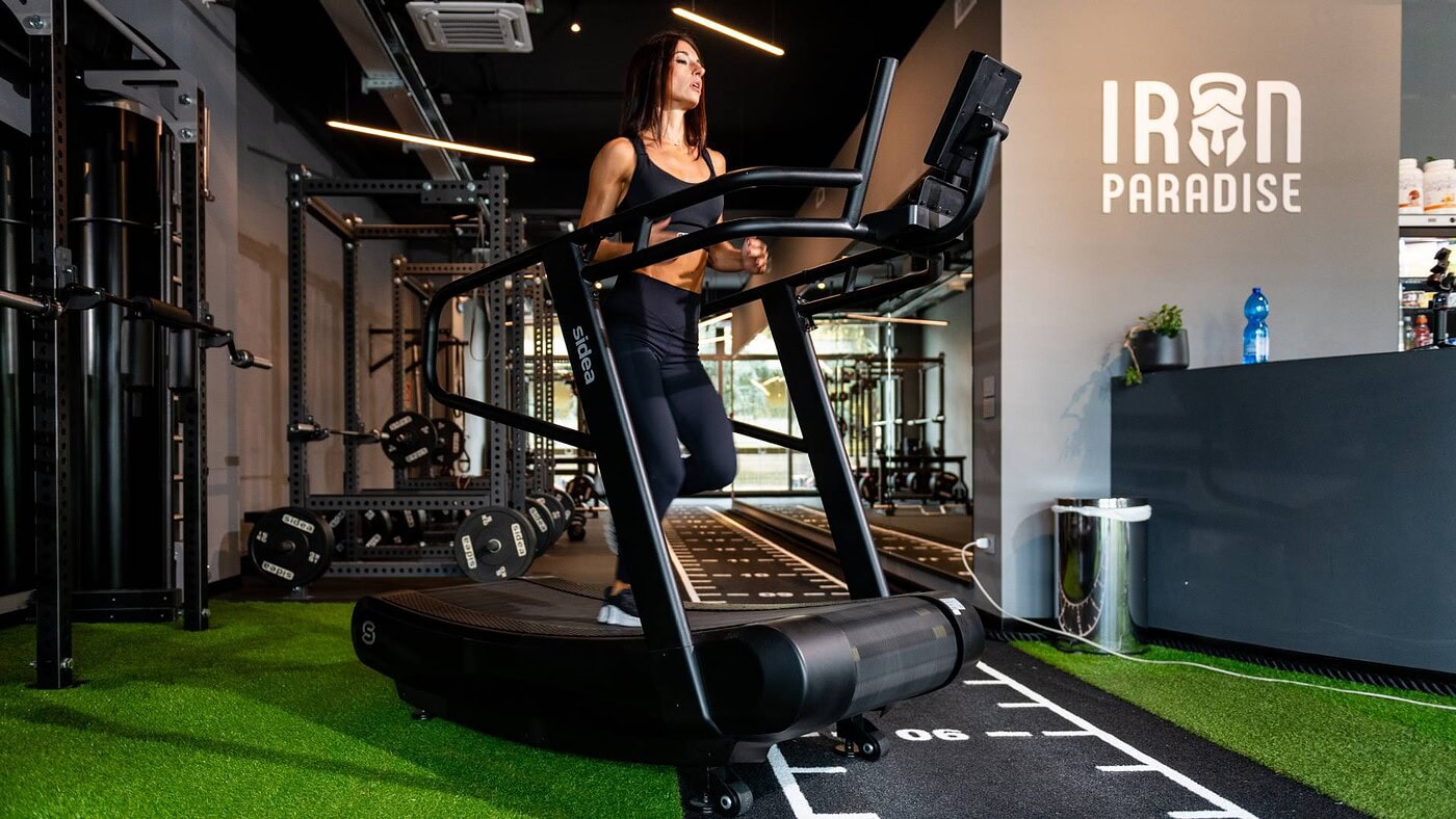Donna che corre su un tapis roulant professionale in palestra, con attrezzature fitness moderne e ambiente ben illuminato, ideale per allenamenti di resistenza e performance.