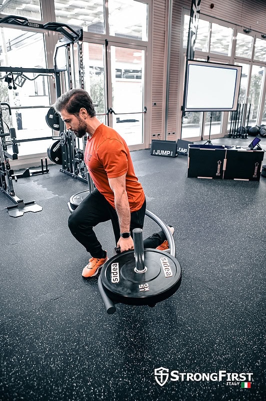 Uomo che solleva un peso con manubri in un centro fitness moderno, attrezzature professionali per allenamento di forza e fitness.