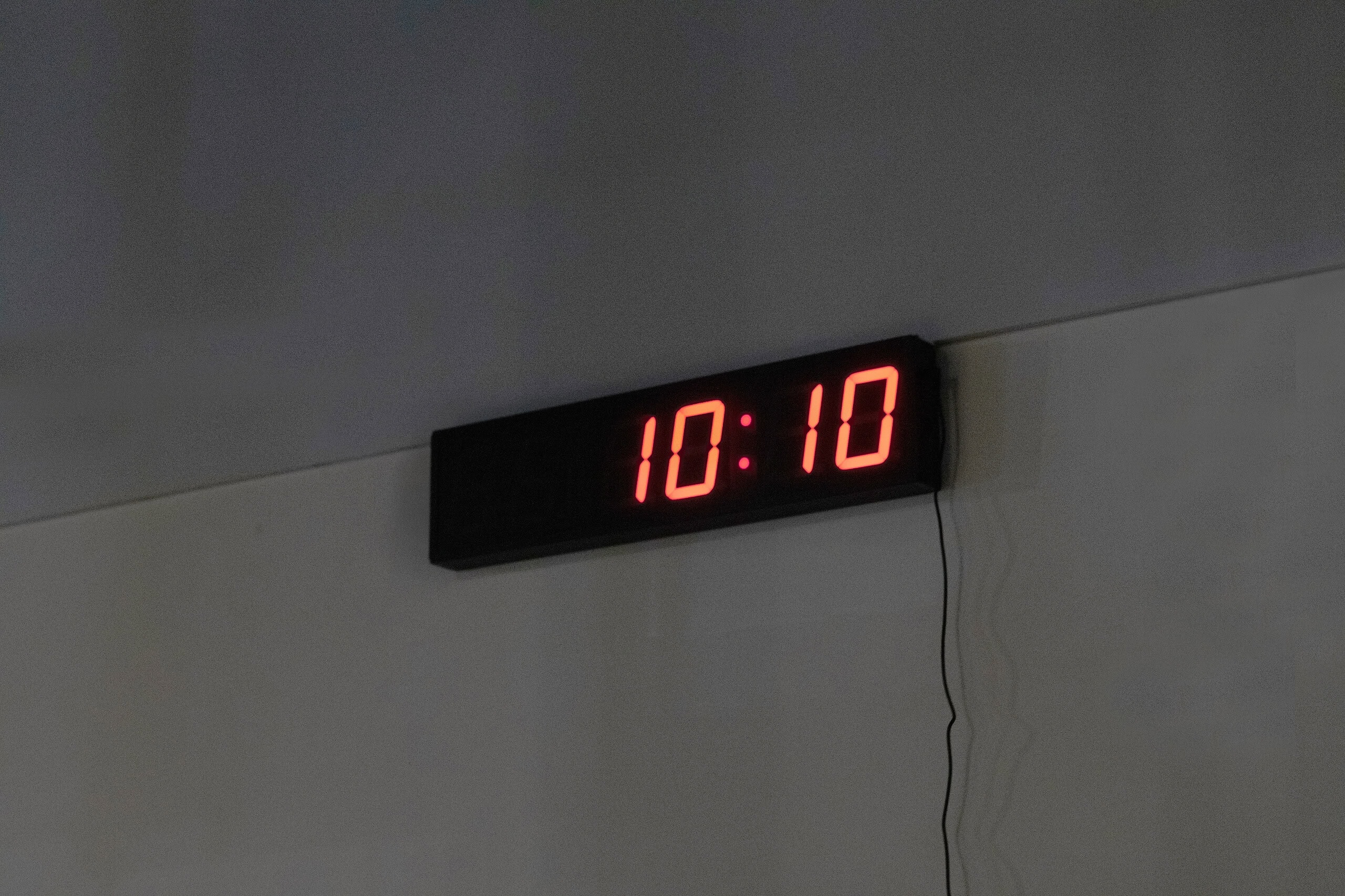 Orologio digitale a LED rosso che mostra le 10:10, installato su parete bianca.